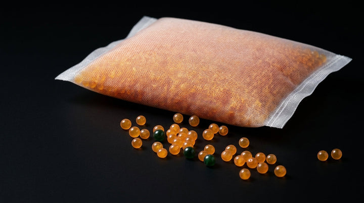 SilicaBox mesh pouch filled with orange silica gel beads on black, loose beads scattered in front