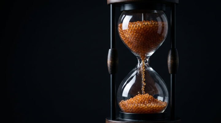 Hourglass filled with orange silica gel beads running through the neck, on black