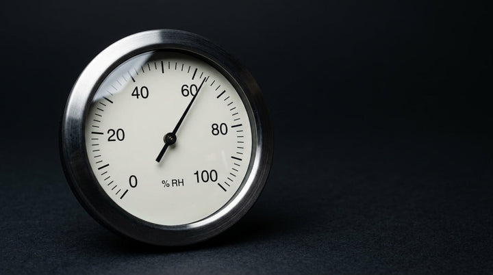 Analog hygrometer on black with the needle just past 60 percent relative humidity
