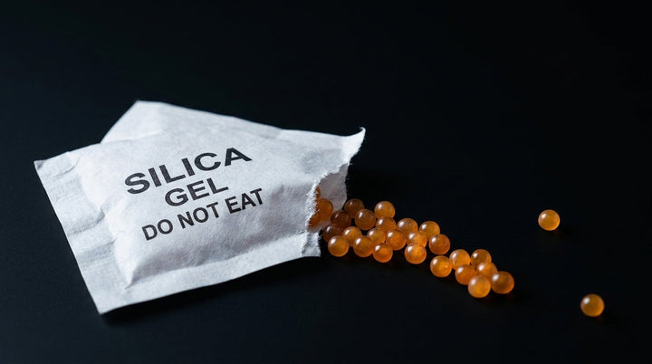 Torn white desiccant packet printed SILICA GEL DO NOT EAT with orange beads spilling out, macro on black