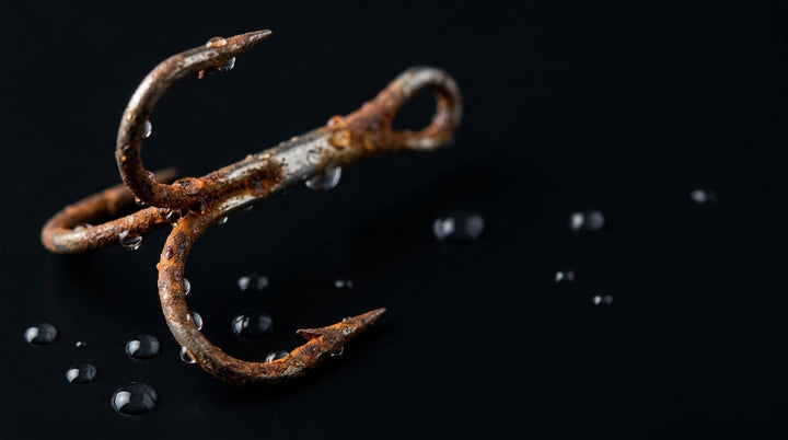 Rusty fishing treble hook surrounded by condensation droplets, macro on black